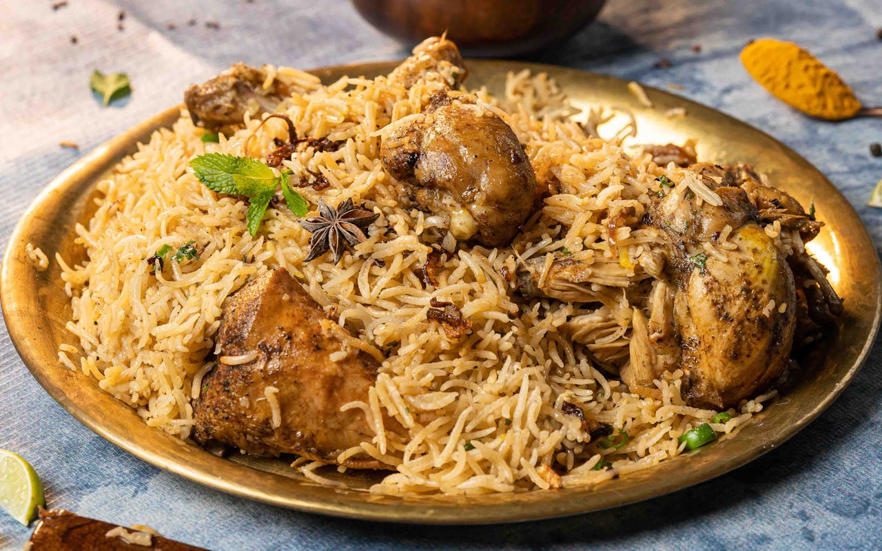 gallery-4 Close-up of aromatic chicken biryani served on a brass plate with garnishes, showcasing Indian culinary art.