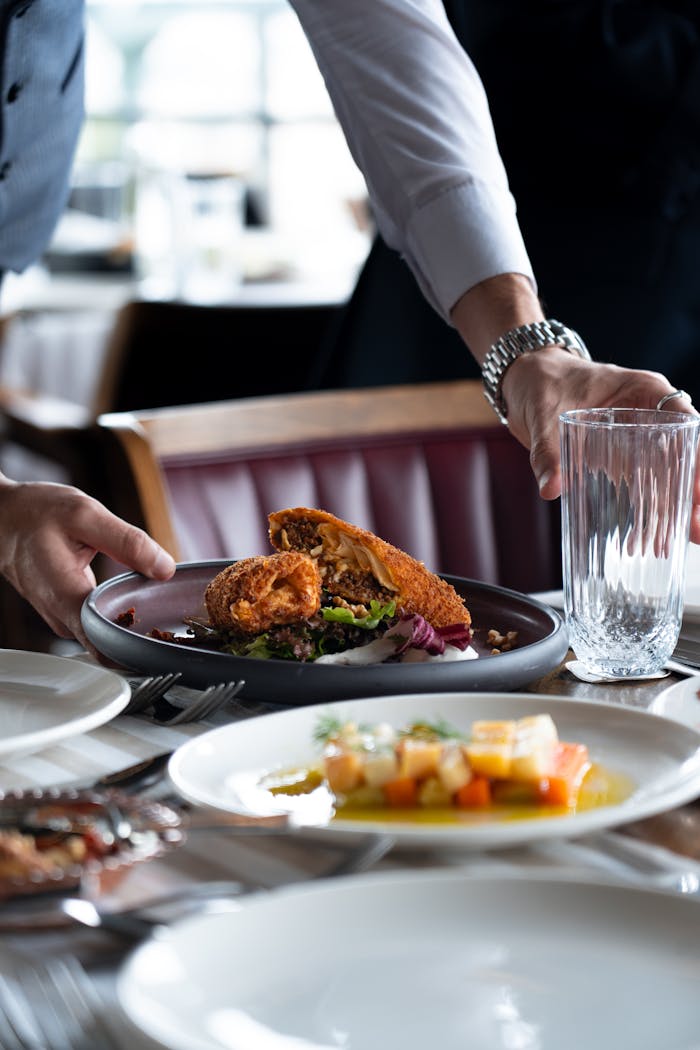 about-01 A waiter serves a plate of crispy fried chicken with mixed vegetables at a restaurant table.