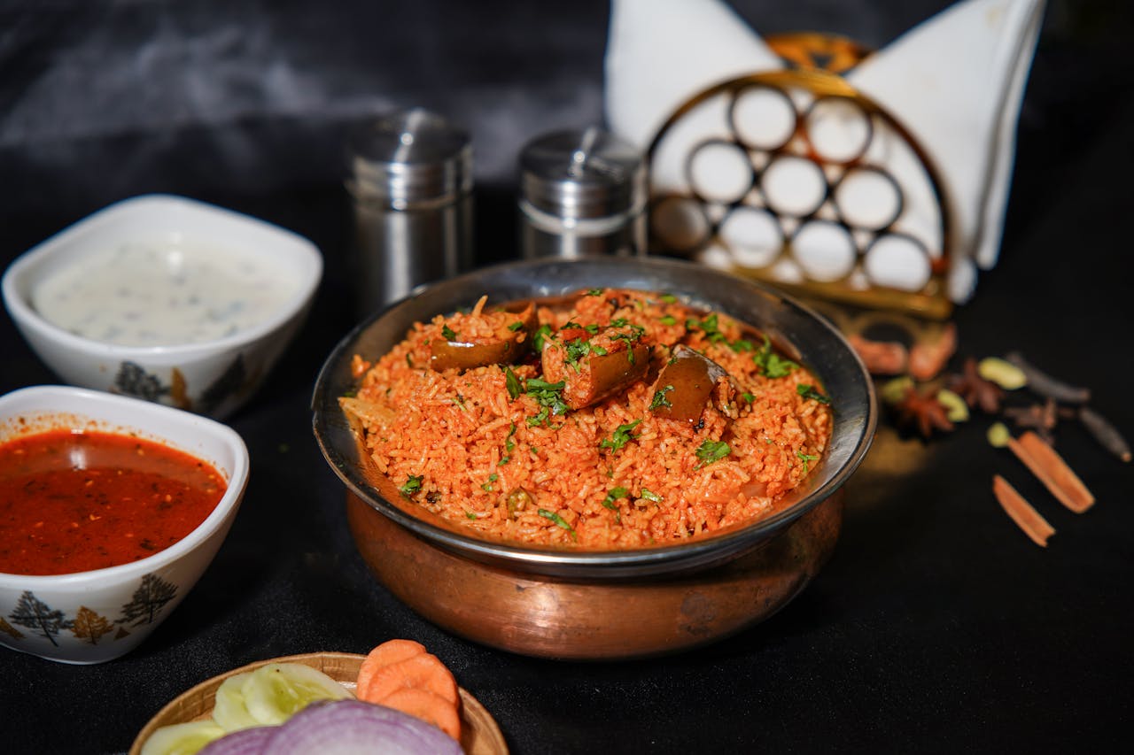 services-01 Delicious traditional Indian biryani served with spices, yogurt sauce, and colorful vegetables.