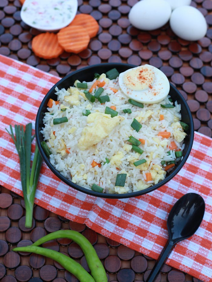gallery-3 Colorful Asian fried rice with eggs and vegetables on a checked cloth, garnished with herbs.