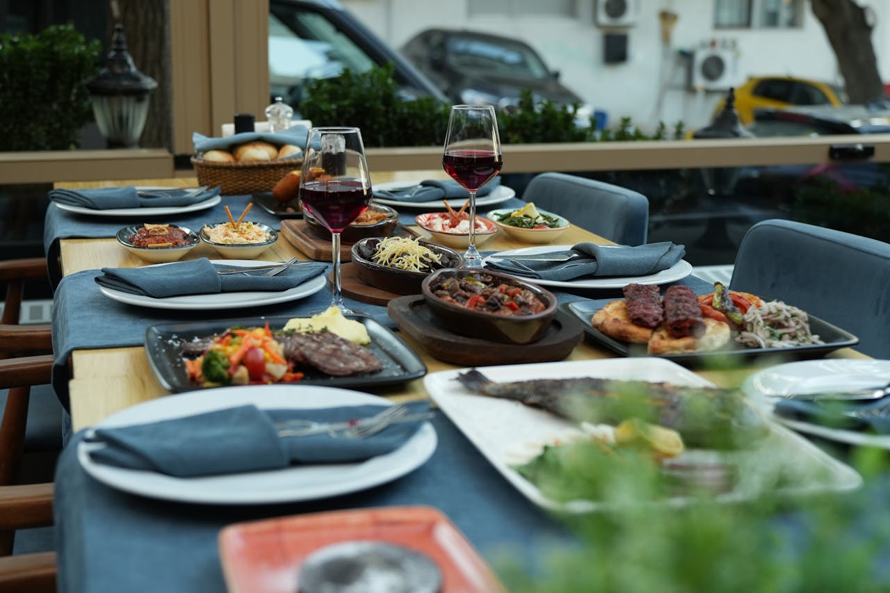 A lavish spread of diverse dishes on an outdoor dining table with wine glasses.