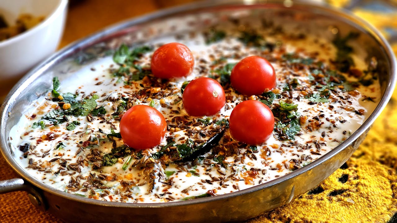 Indian raita with cherry tomatoes, spices, and herbs in a metal dish.