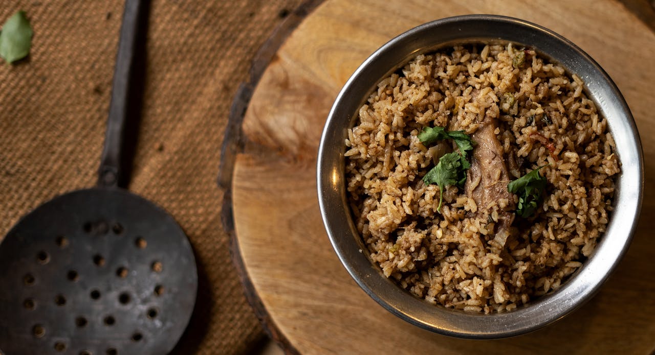 services-02 Top view of spiced rice with meat in a metal bowl on a rustic wooden surface.